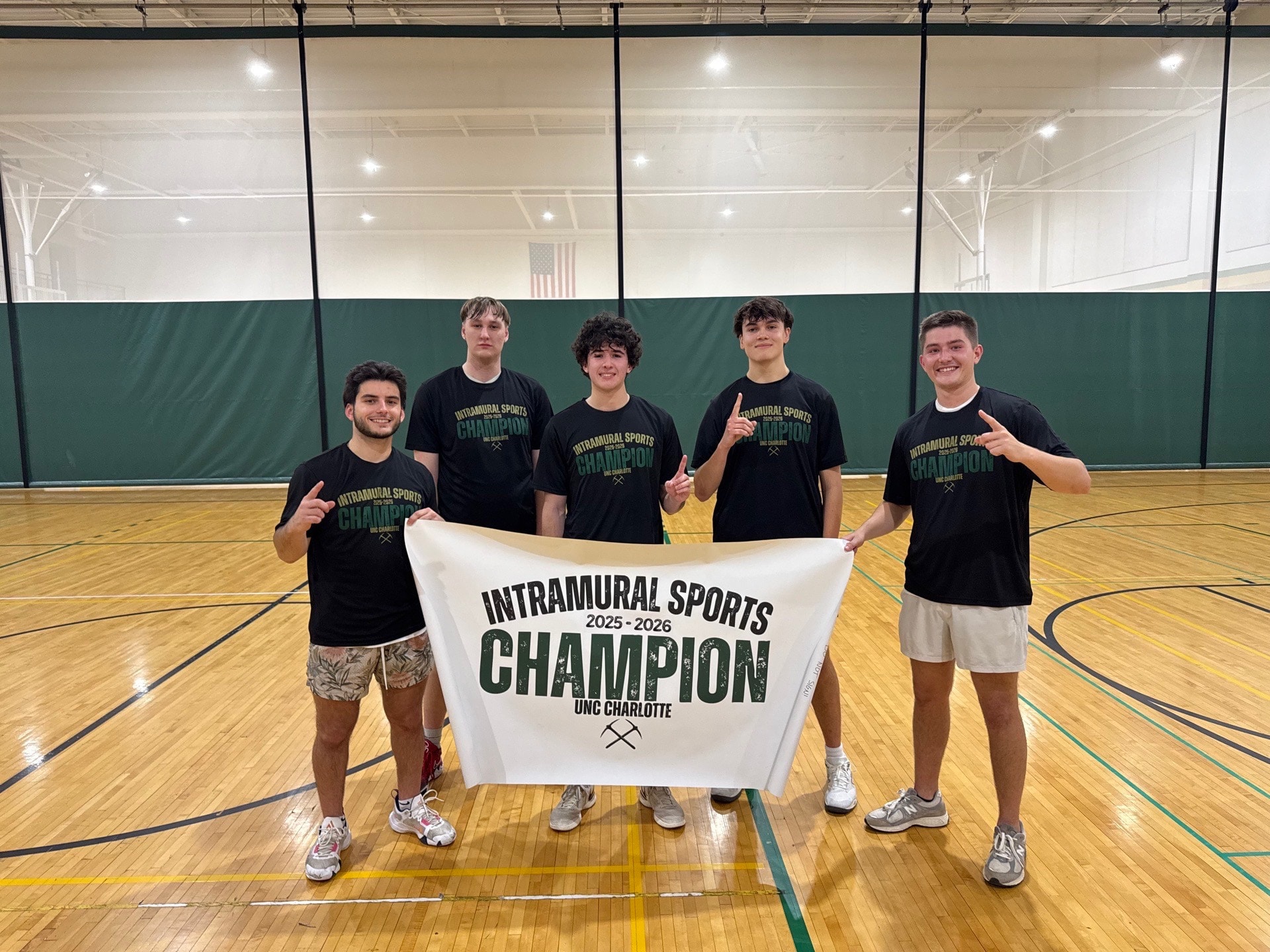Five NC Epsilon brothers in a campus gym holding an Intramural Sports Champion banner